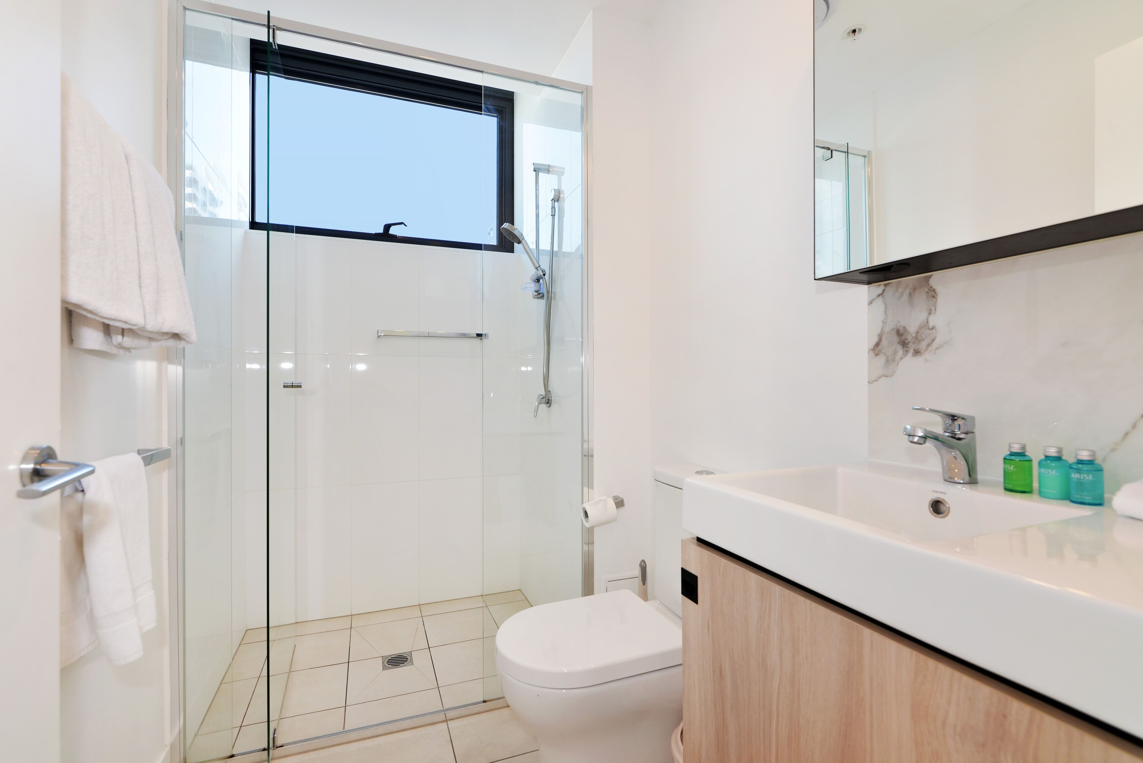 Une salle de bain moderne avec une douche à parois de verre, des toilettes blanches et un lavabo doté d’un plan de travail en marbre.