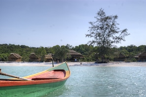 A boat on calm water with thatched-roof huts in the background.