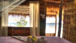 Una habitación con cama, ventana con vista al mar y techo de paja.