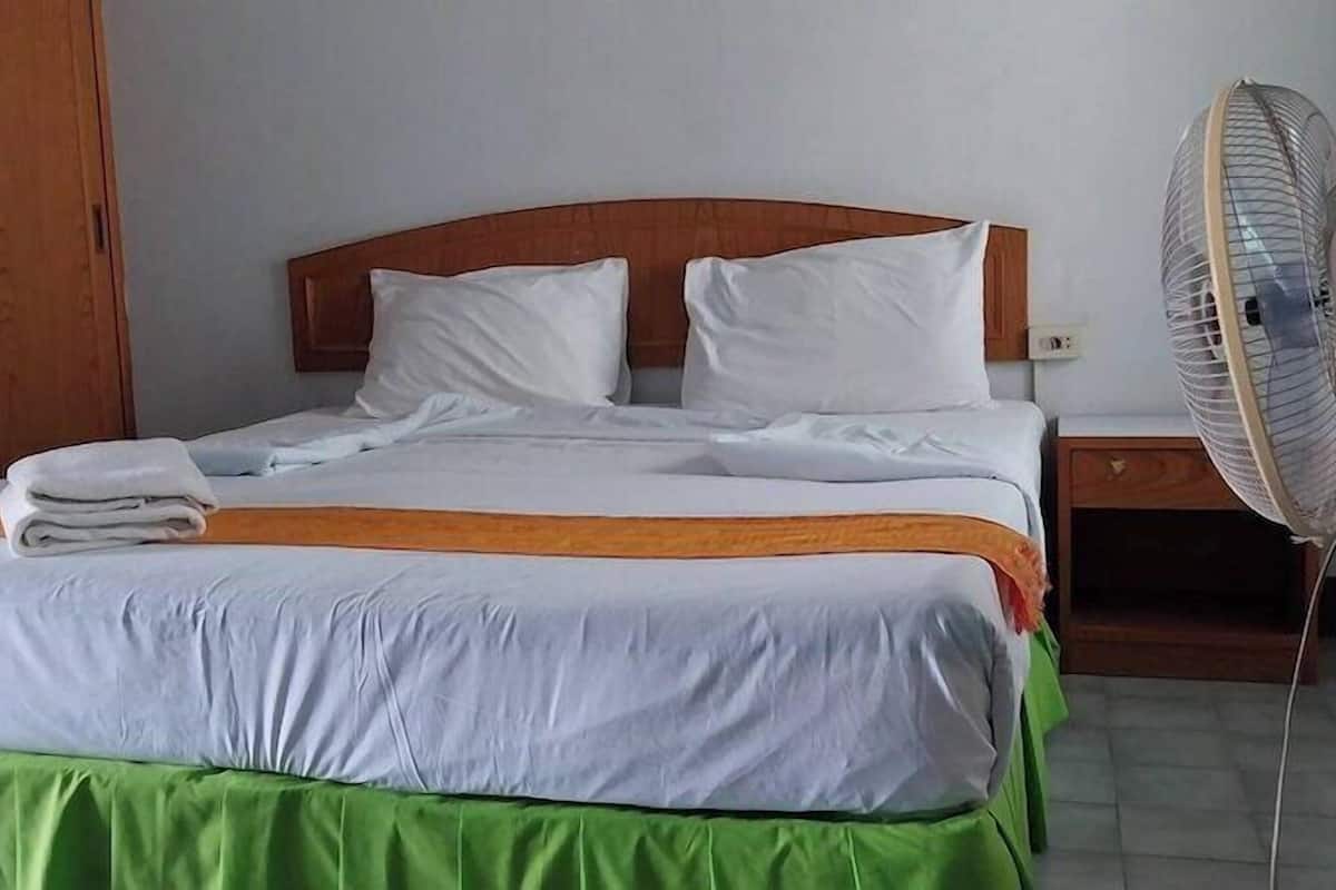 A bed with white and green bedding, a wooden headboard, a bedside table, and a standing fan.