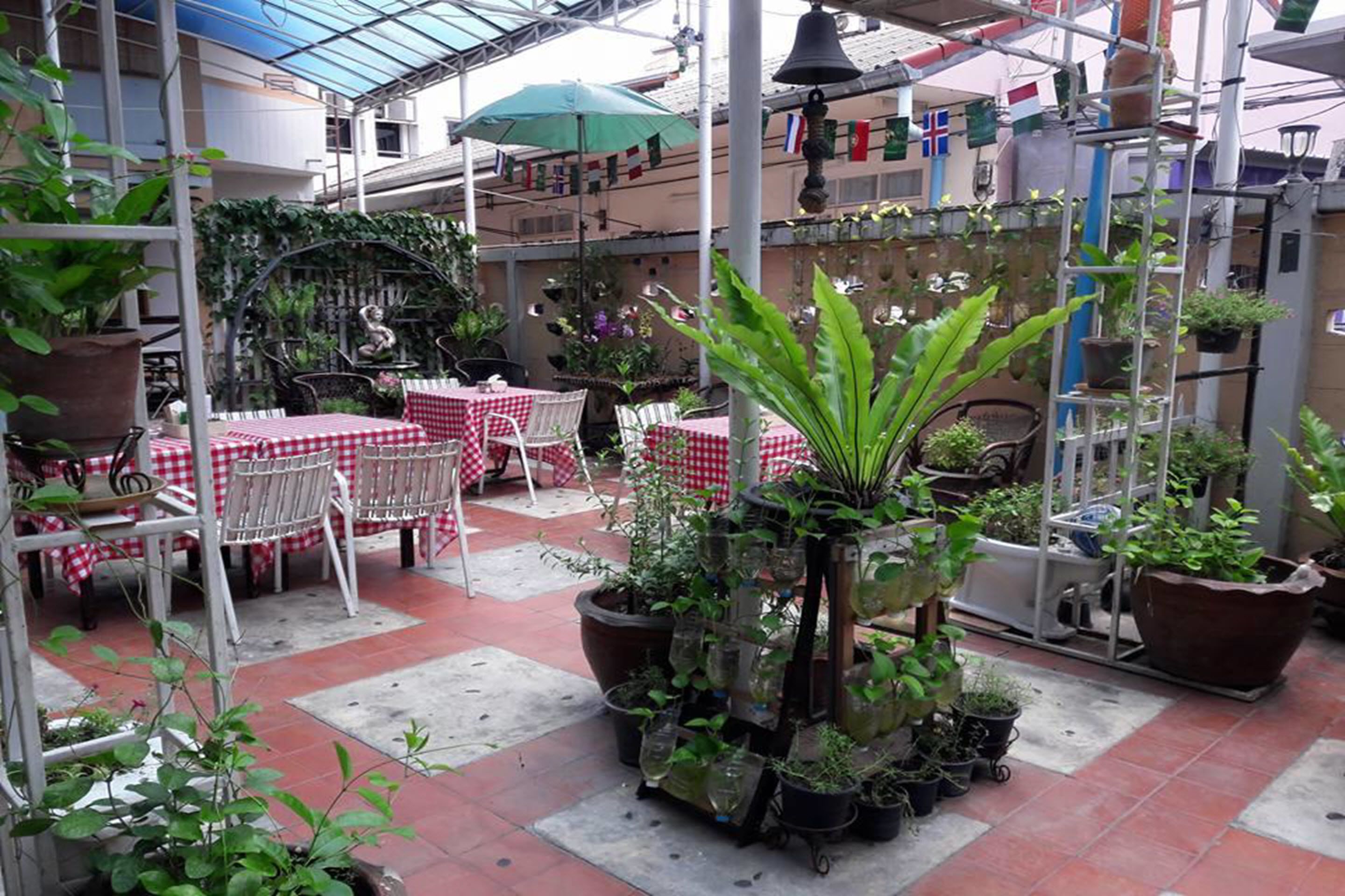 Zona de pati exterior amb taules i caires, plantes en testos i una campana penjada d'un pal.