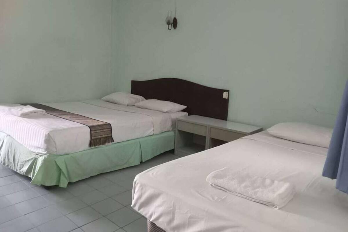 A room with two beds, each with a pillow and a blanket, a bedside table, and a wall-mounted light fixture.
