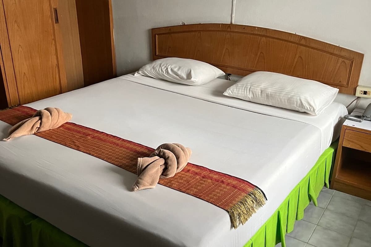 A neatly made bed with a green skirt, white linens, and two towels.