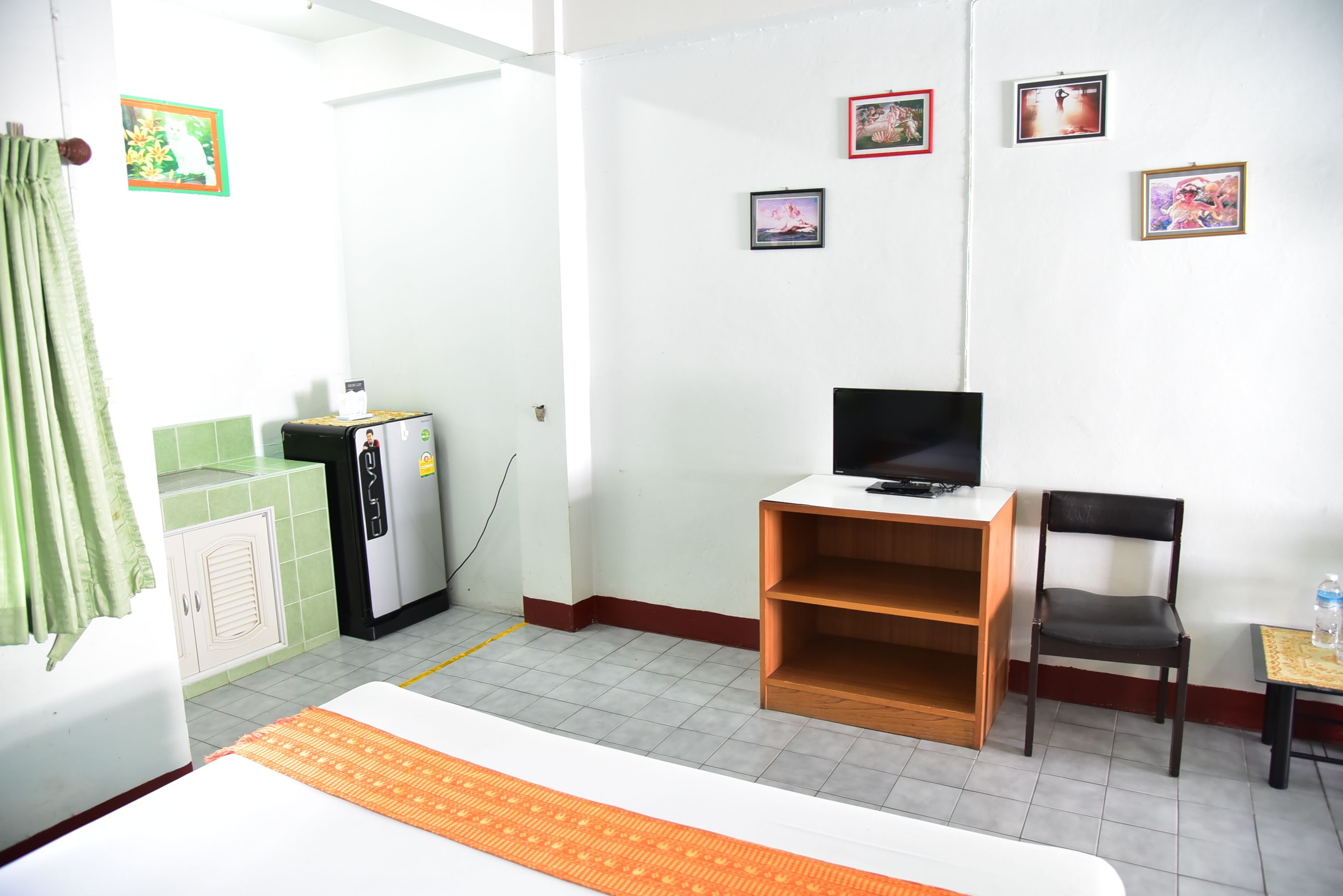 A hotel room with a bed, a desk, a chair, a television, and a refrigerator.