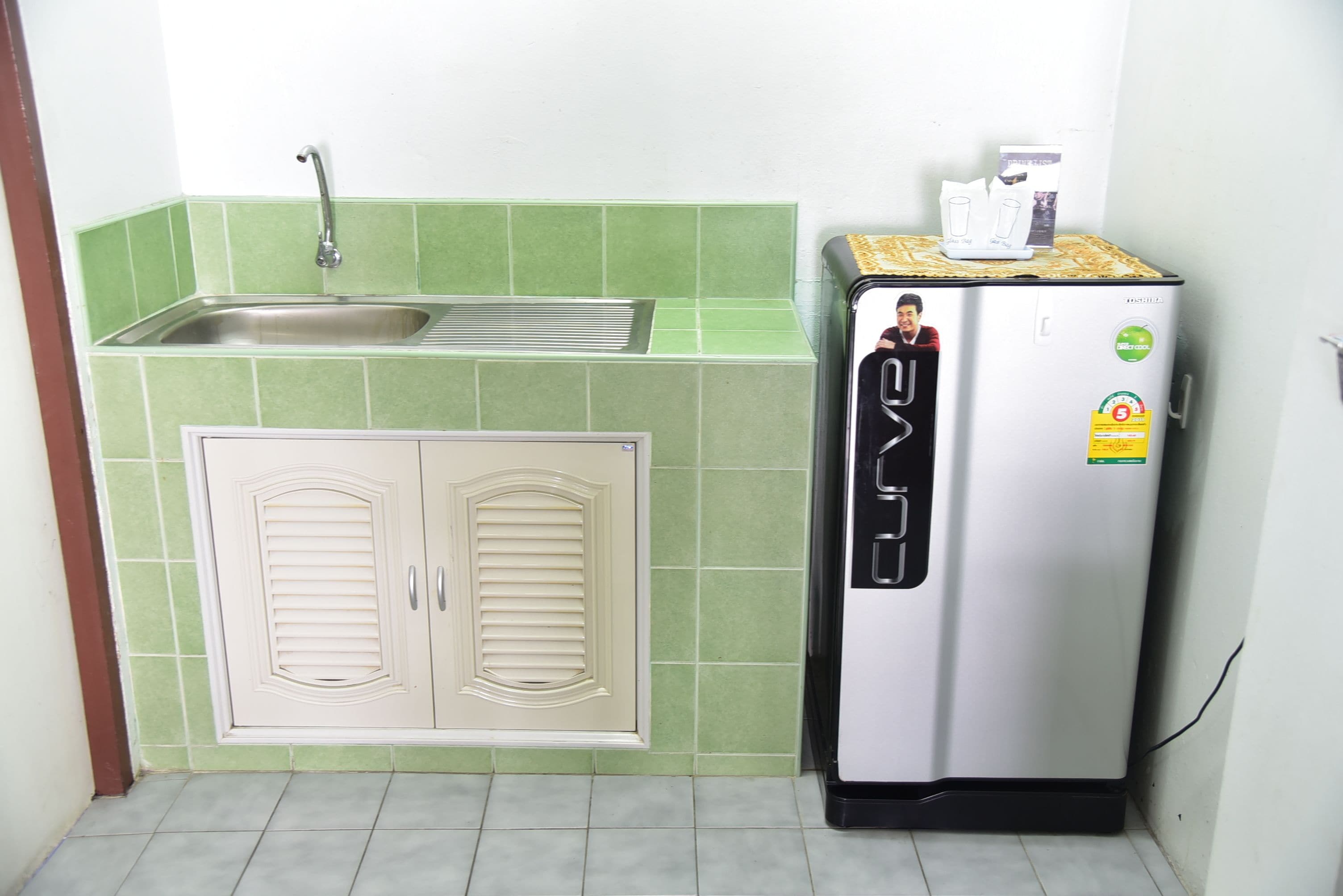 A compact kitchen with a sink, two cabinets, and a refrigerator.