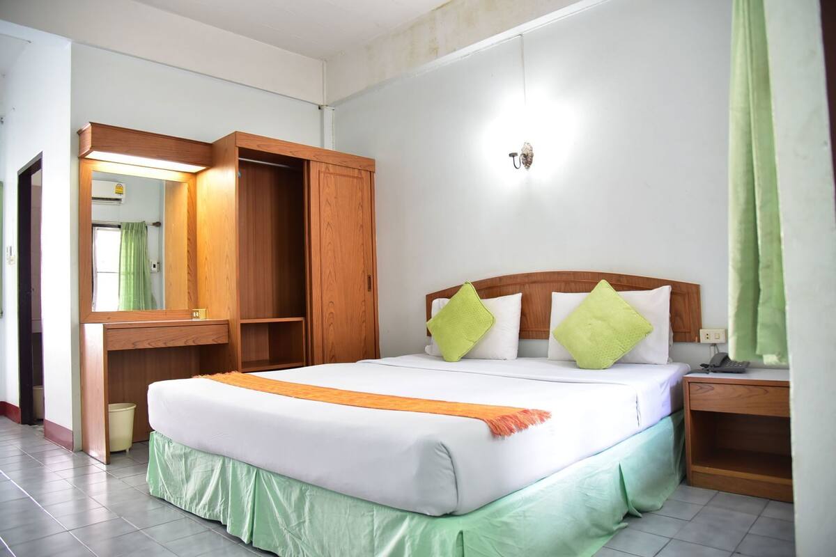 A hotel room with a bed, a wooden wardrobe, a bedside table, and a nightstand.
