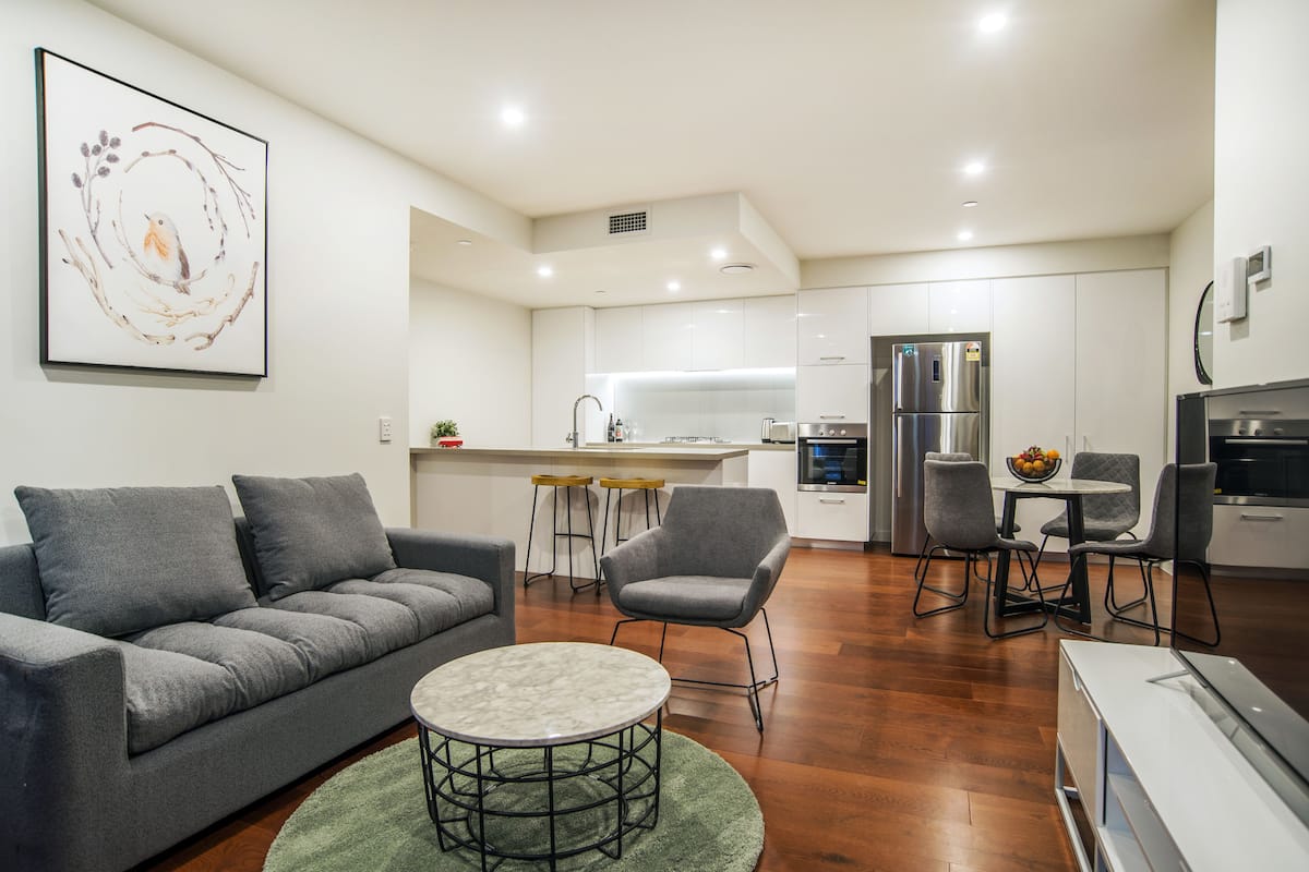 A modern living room with a grey sofa, a round coffee table, and a dining area with a small table and chairs.