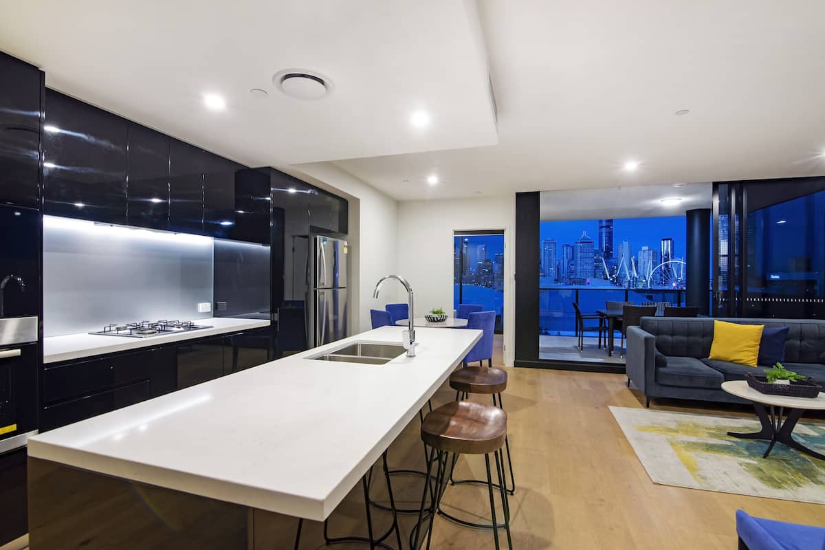 A modern kitchen with a central island, a dining area with a sofa and chairs, and a view of a cityscape through large windows.