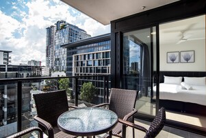 Un balcone con sedie in vimini e un tavolo in vetro, con vista su un panorama urbano caratterizzato da edifici moderni.