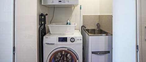 A compact laundry area with a front-loading washer and dryer, a small sink, and a basket on the dryer.