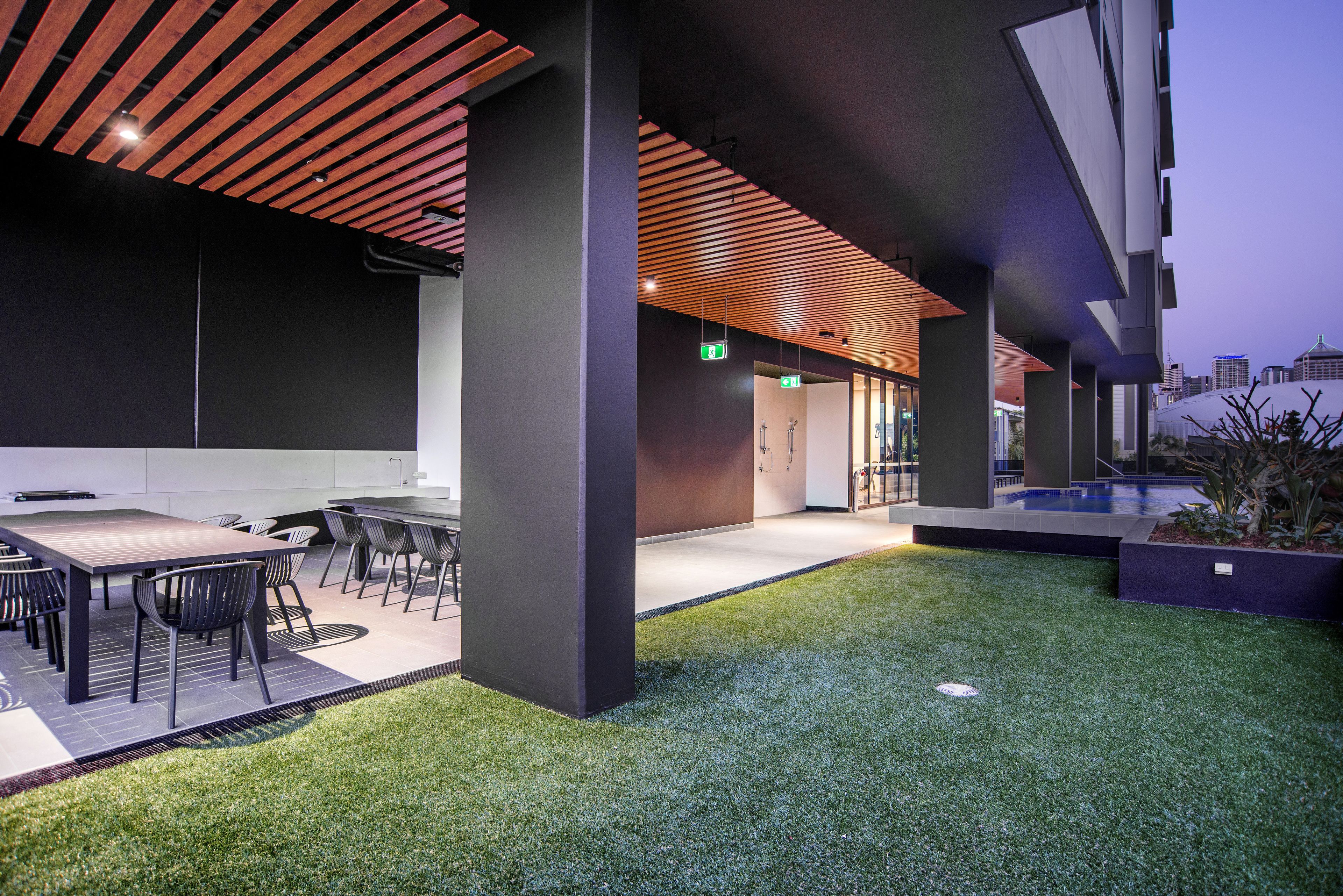 An outdoor dining area with a wooden ceiling, artificial grass, and modern furniture.