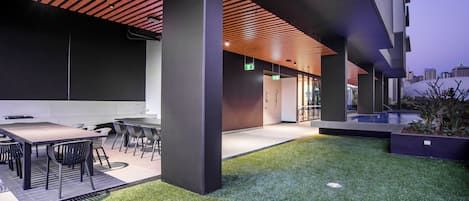 Un área de comedor al aire libre con techo de madera, césped artificial y mobiliario moderno.