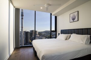 Una camera da letto con un letto grande, un ventilatore a soffitto e vista sulla città attraverso ampie finestre a tutta altezza.