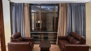 Una sala de estar con dos sofás de cuero marrón, una mesita de madera y un ventanal con cortinas.