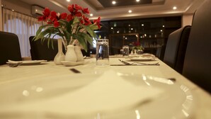 Mesa de comedor con mantel blanco, flores rojas y cristalería transparente.