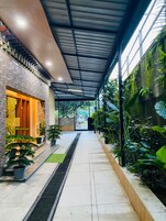 Uma galeria coberta com uma parede de tijolos de um lado e uma parede verde do outro, repleta de plantas em vasos.