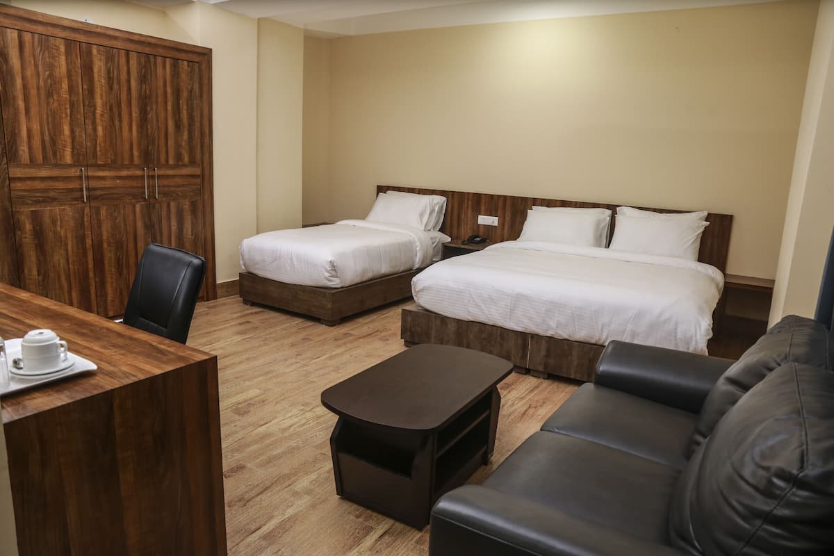 Hotellihuone, jossa on kaksi sänkyä, puinen vaatekaappi, työpöytä tuolilla ja pieni pöytä.