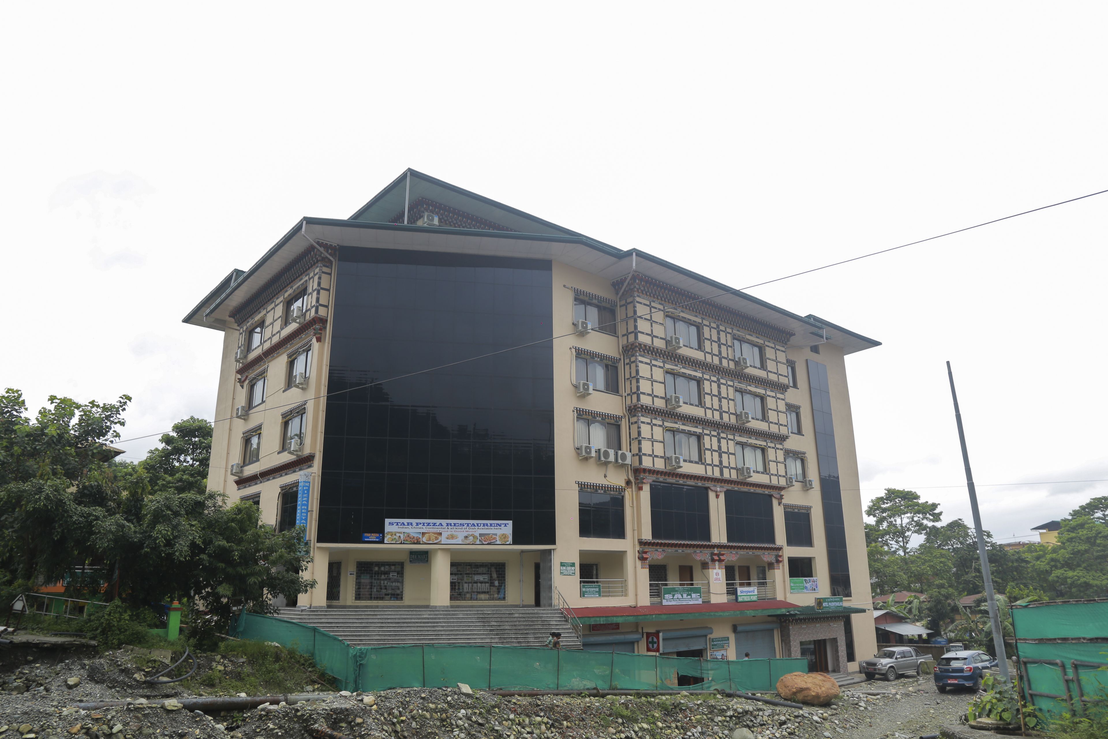 A multi-story building with a large glass facade, a sign for a Star Pizza Restaurant, and a green construction barrier in front.