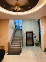Um saguão de hotel com uma escada, um balcão de recepção e uma porta com a inscrição 'Lobby'.