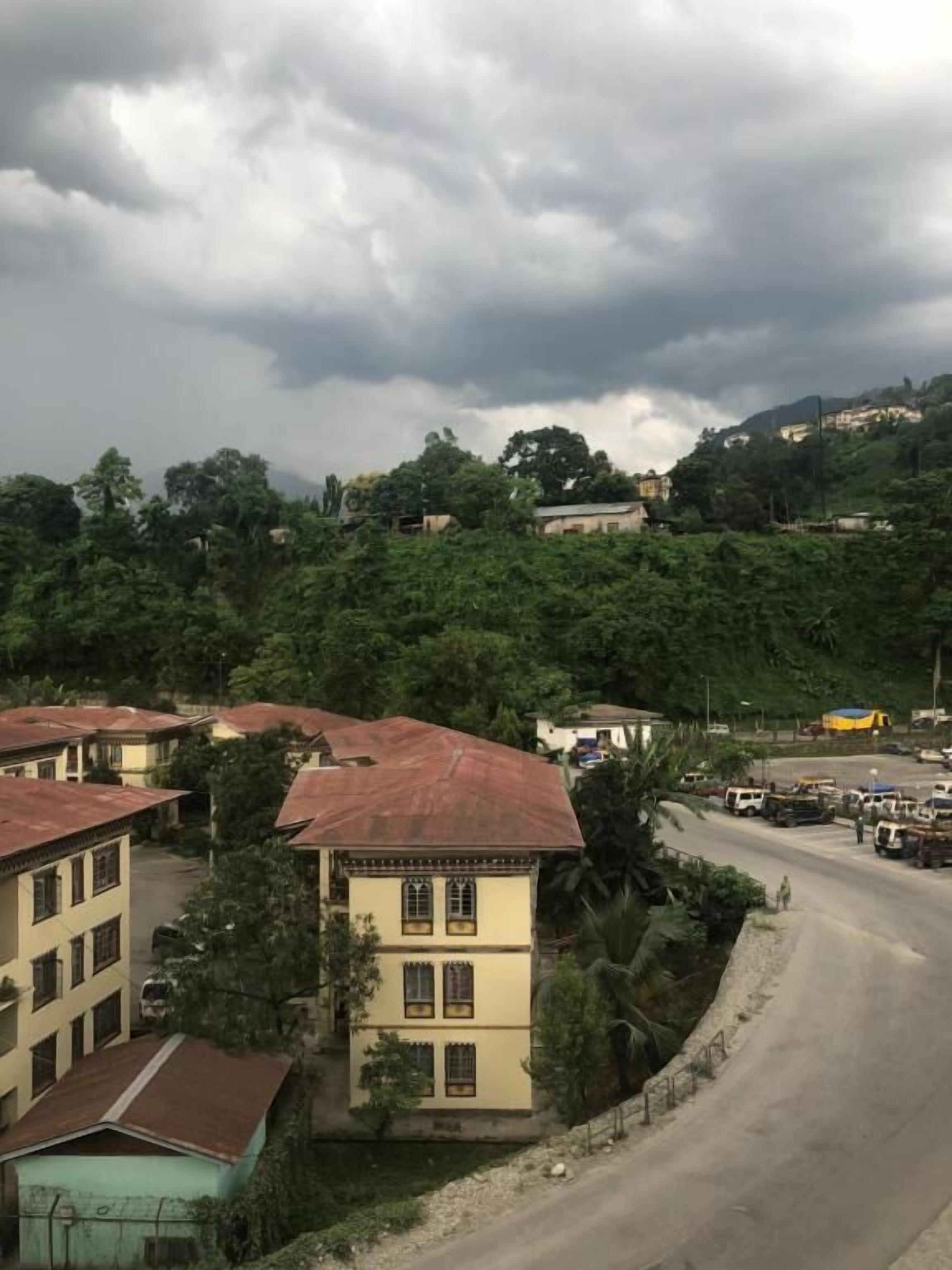 A residential area with buildings, a winding road, and a hilly backdrop.