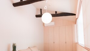 A bedroom with a wooden floor, a bed with white bedding, a small wooden nightstand, a potted plant, and a hanging light fixture. - Yaoya Kyoto Kyomizu Gojo (Kyoto)