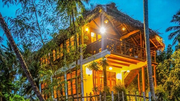 A two-story building with a thatched roof, surrounded by water and vegetation. - Milkyway Holiday Resort (Unawatuna)