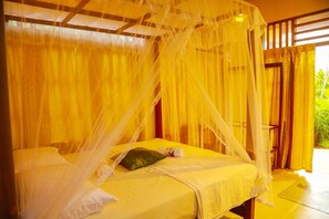 A room with a bed covered by a canopy, a pillow, and a small table with a bottle.