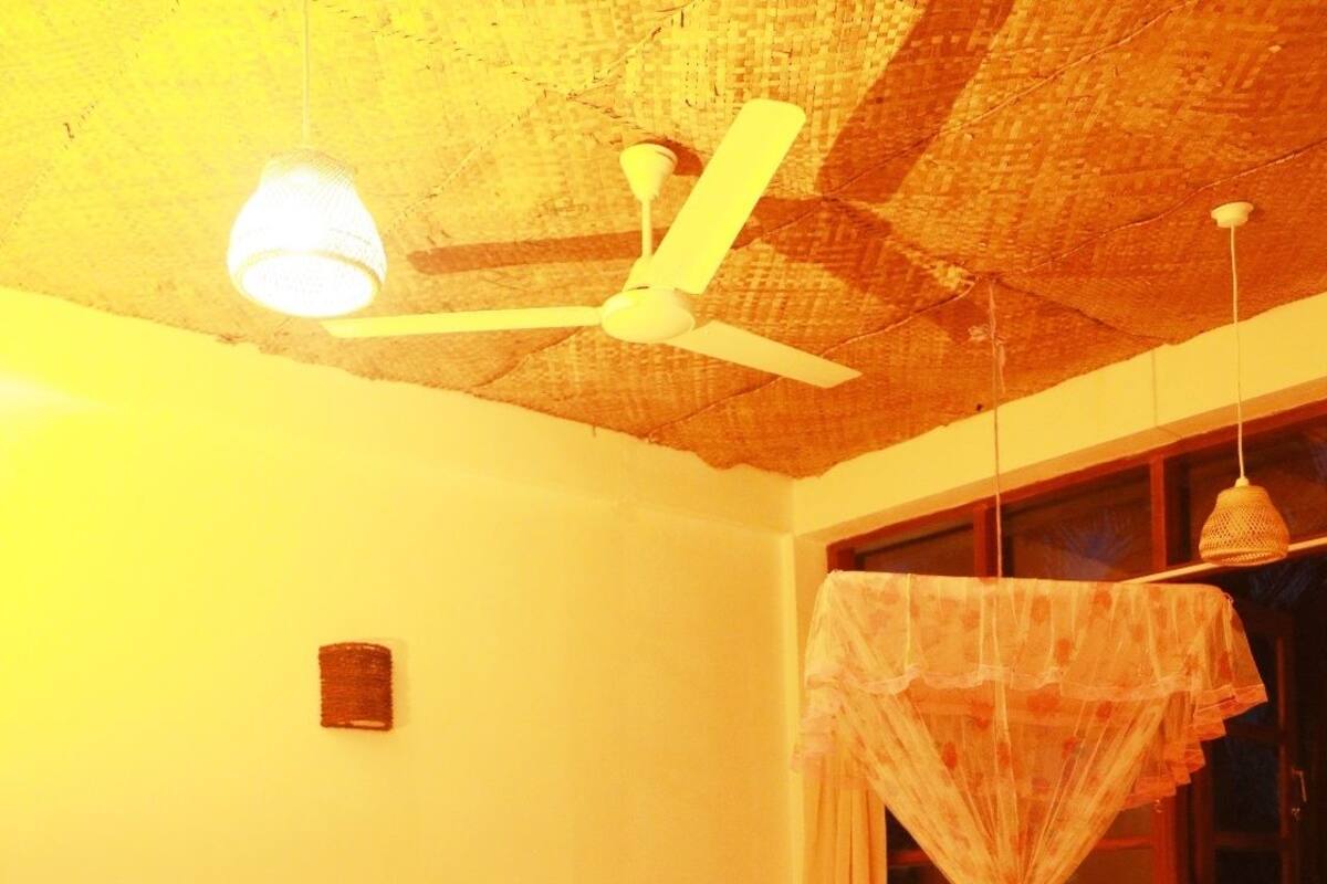 A room with a bed, a chair, a ceiling fan, and a window with a curtain.