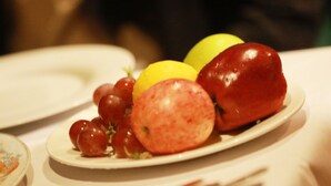 A plate with red grapes, a yellow lemon, and a red apple on a white tablecloth. - Milkyway Holiday Resort (Unawatuna)