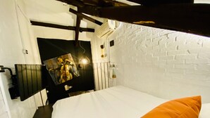 A hotel room with a white brick wall, a bed with an orange pillow, a mounted TV, and a hanging light fixture. - Zhengxing Yanping Homestay (Tainan)