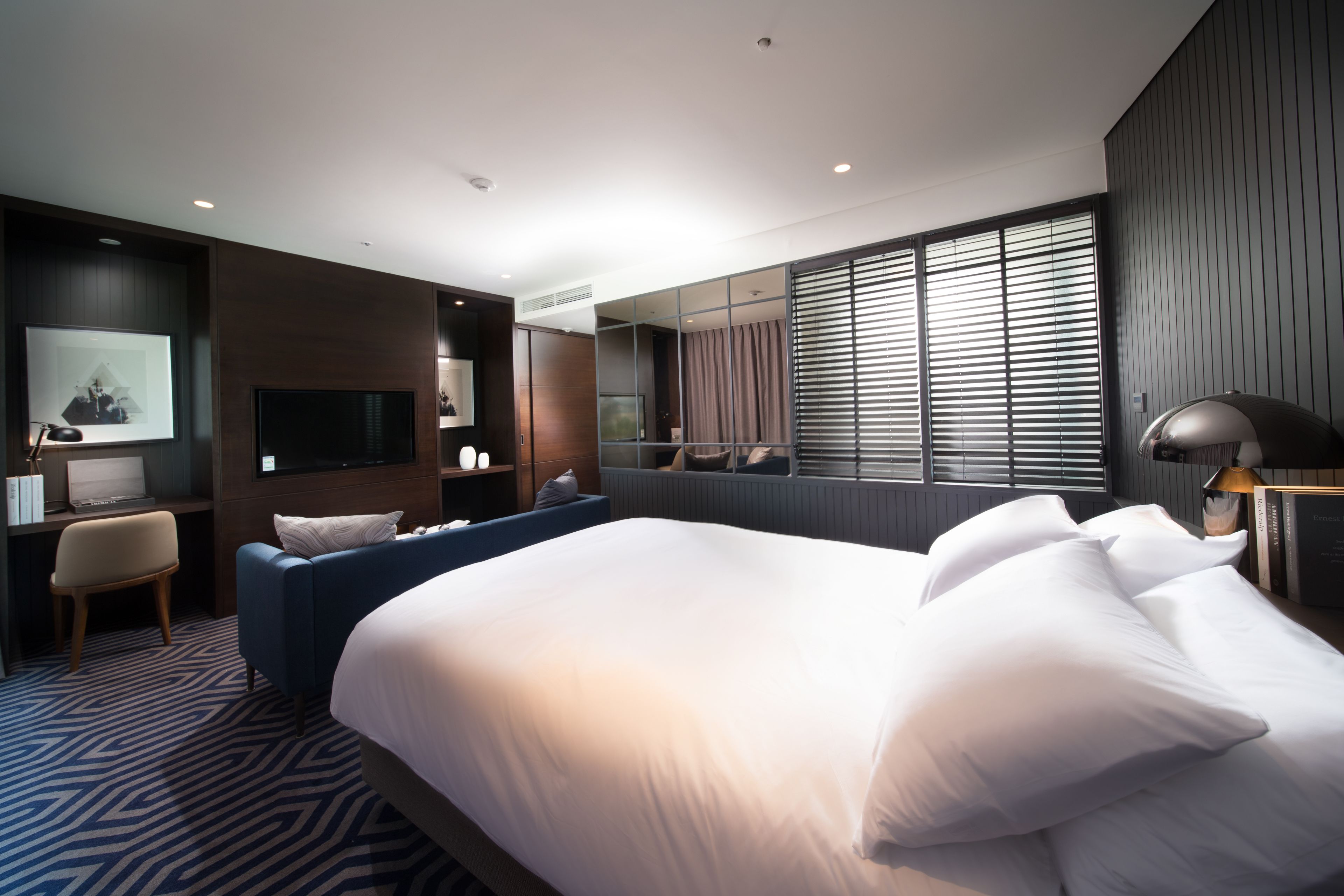 A modern hotel room with a large bed, a seating area, a desk, and a television.