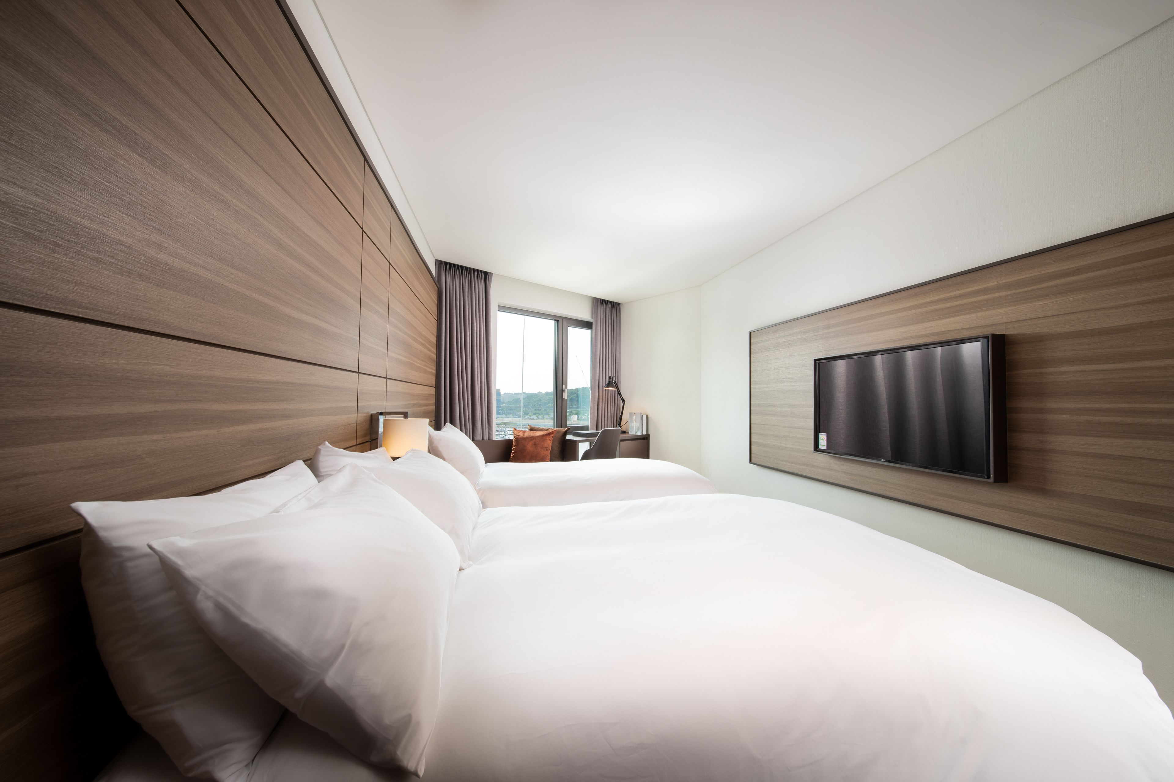 Een hotelkamer met twee bedden, een aan de muur bevestigde televisie en een raam met gordijnen.