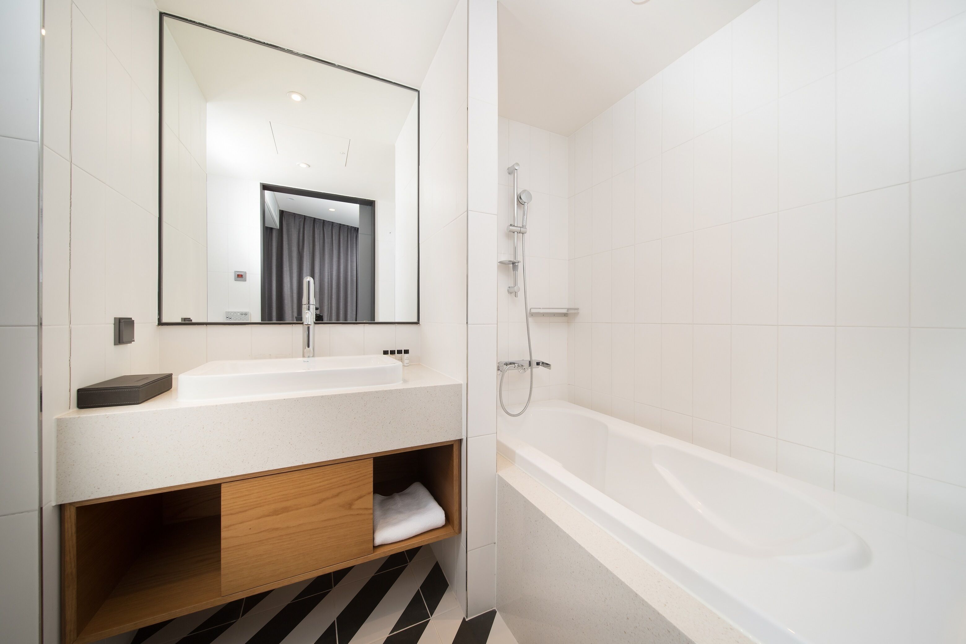 Un baño moderno con un lavamanos blanco, un espejo grande, un mueble de tocador de madera y una bañera blanca.