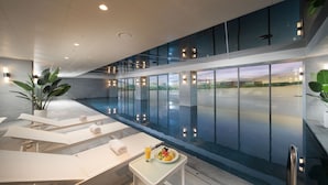 Un espace piscine intérieur moderne, doté de chaises longues et d'une table sur laquelle est disposée une assiette de fruits.