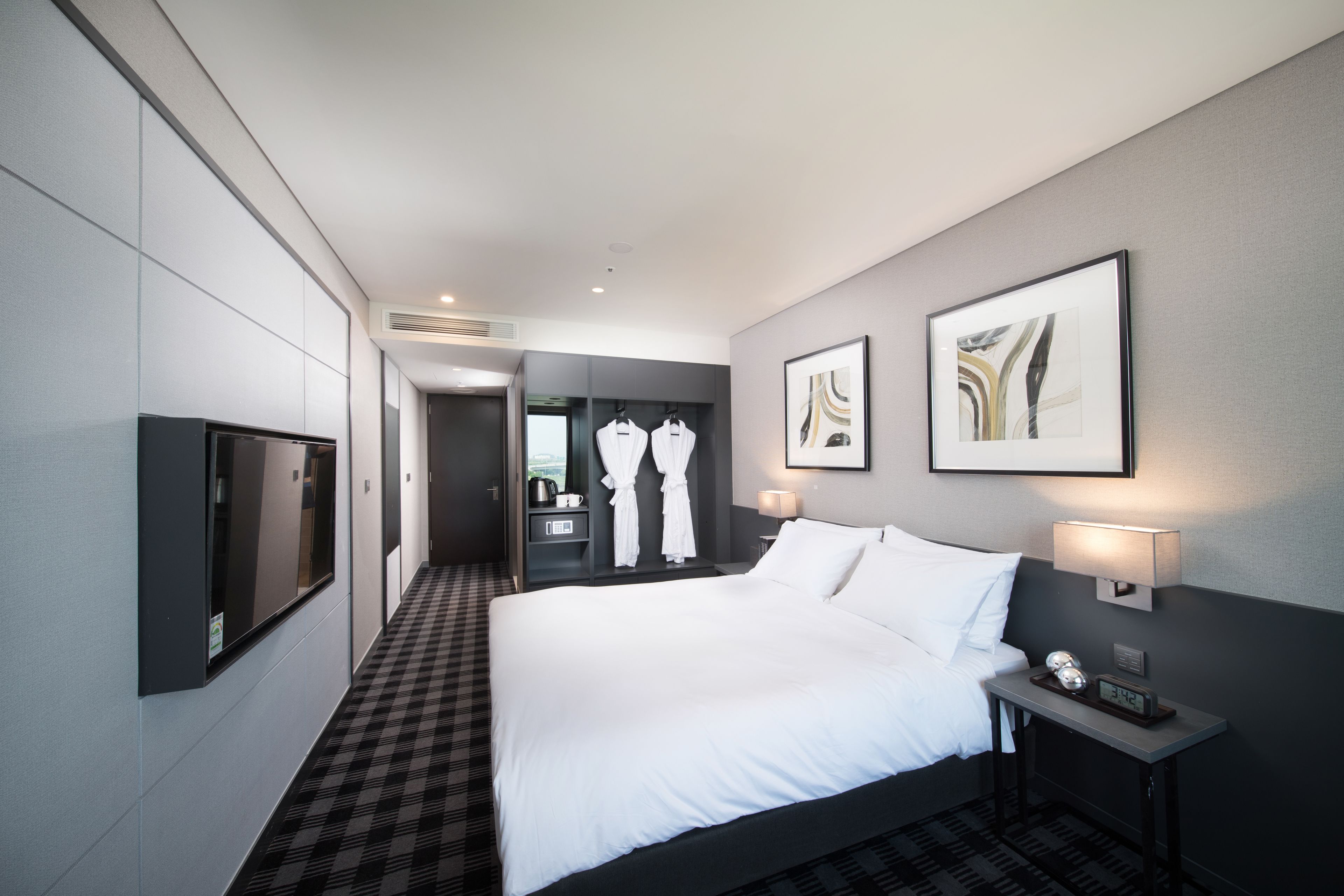 A hotel room with a large bed, a flat-screen TV, a bedside table with a lamp, and a framed picture on the wall.