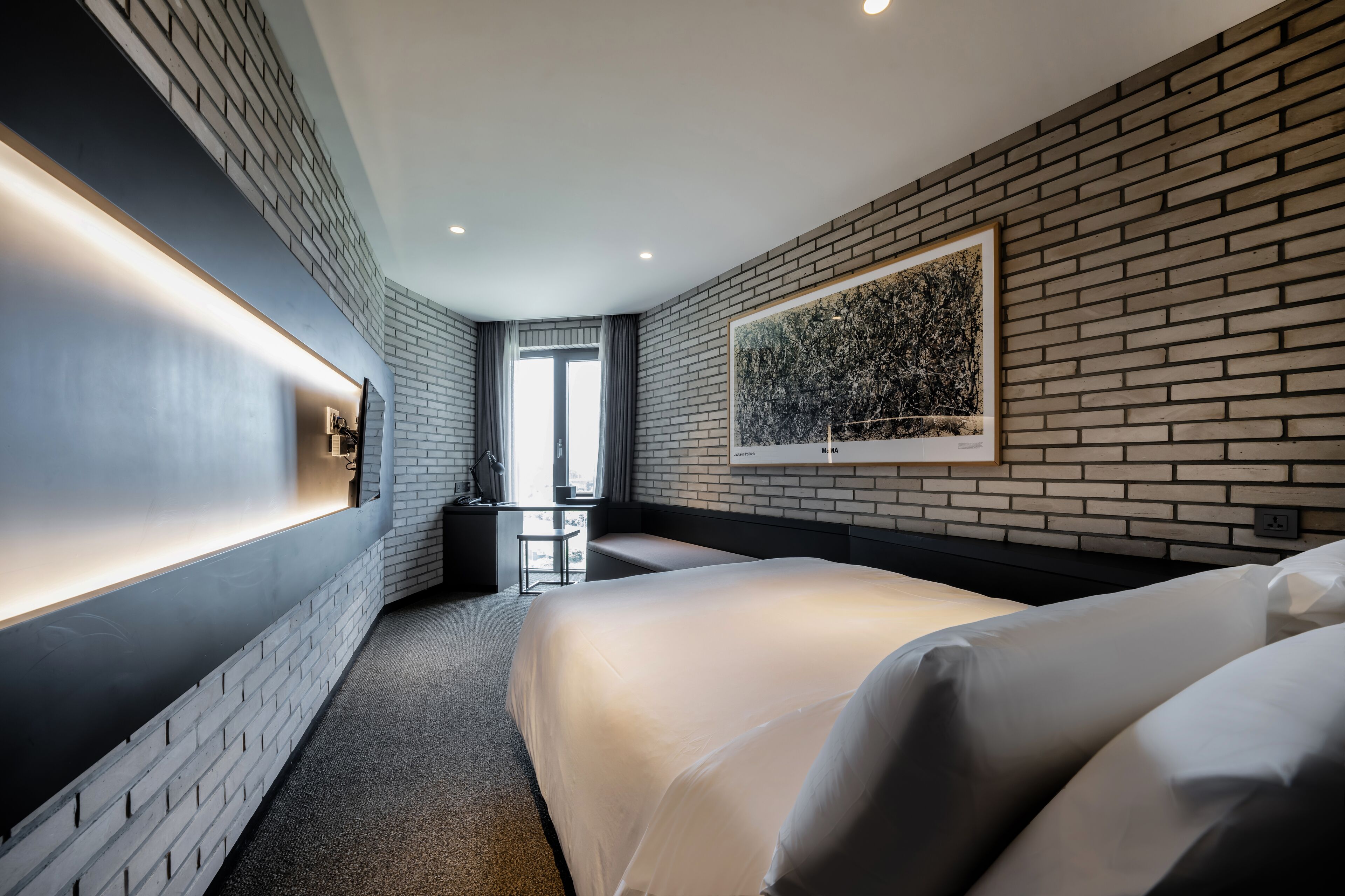 Una habitación de hotel moderna con pared de ladrillo, una cama grande, un escritorio y una ventana con cortinas.