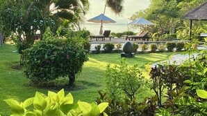 A tropical garden with palm trees, a thatched-roof structure, and a pool area with lounge chairs. - Direct beachfront 4BR/BR villa in tropical garden. Villa chef, villa pool, WiFi (Umeanyar)