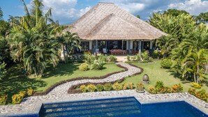 A resort with a thatched-roof building, a swimming pool, and lush tropical gardens. - Direct beachfront 4BR/BR villa in tropical garden. Villa chef, villa pool, WiFi (Umeanyar)