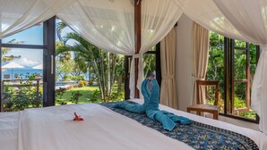 A bedroom with a large bed, a view of a tropical garden, and a wooden chair. - Direct beachfront 4BR/BR villa in tropical garden. Villa chef, villa pool, WiFi (Umeanyar)