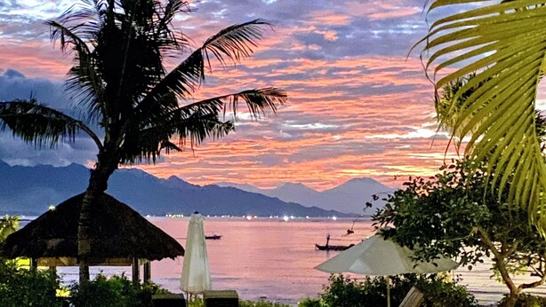 A poolside area with lounge chairs, a palm tree, and a view of the water and mountains. - Direct beachfront 4BR/BR villa in tropical garden. Villa chef, villa pool, WiFi (Umeanyar)