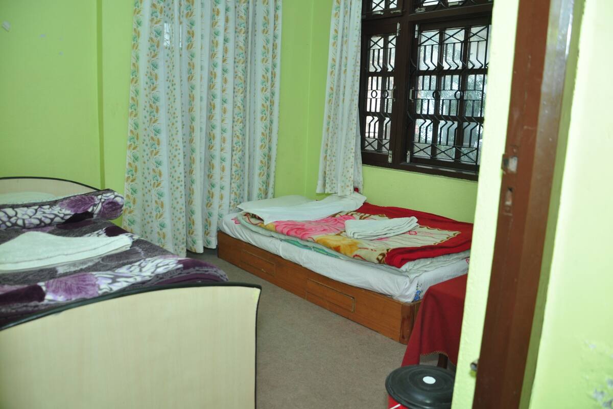 A small bedroom with two beds, a window with bars, and a door.