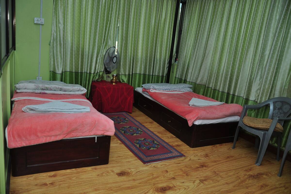 A room with two beds, a fan, a red table, and a chair.