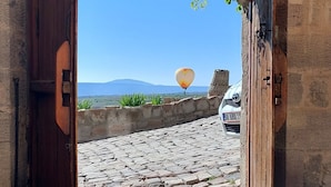 An open doorway leading to a cobblestone courtyard with a clear view of a mountain and a parked car. - Maya Cave Hotel (Nevsehir)