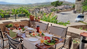 A table set for a meal with a view of a vineyard and mountains in the background. - Maya Cave Hotel (Nevsehir)