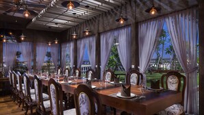 A long dining table set for a meal, surrounded by ornate chairs, with a view of greenery and a building outside. - Le Castle River Hotel & Apartment (Phnom Penh)