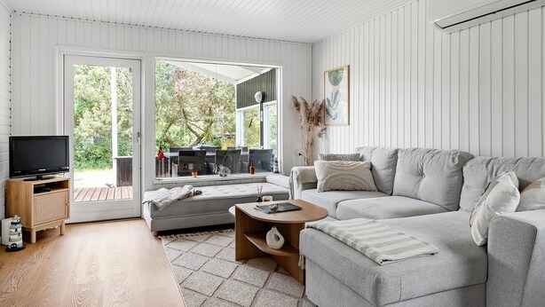 Un salon moderne avec un canapé gris, une table basse en bois et un téléviseur posé sur un meuble en bois.