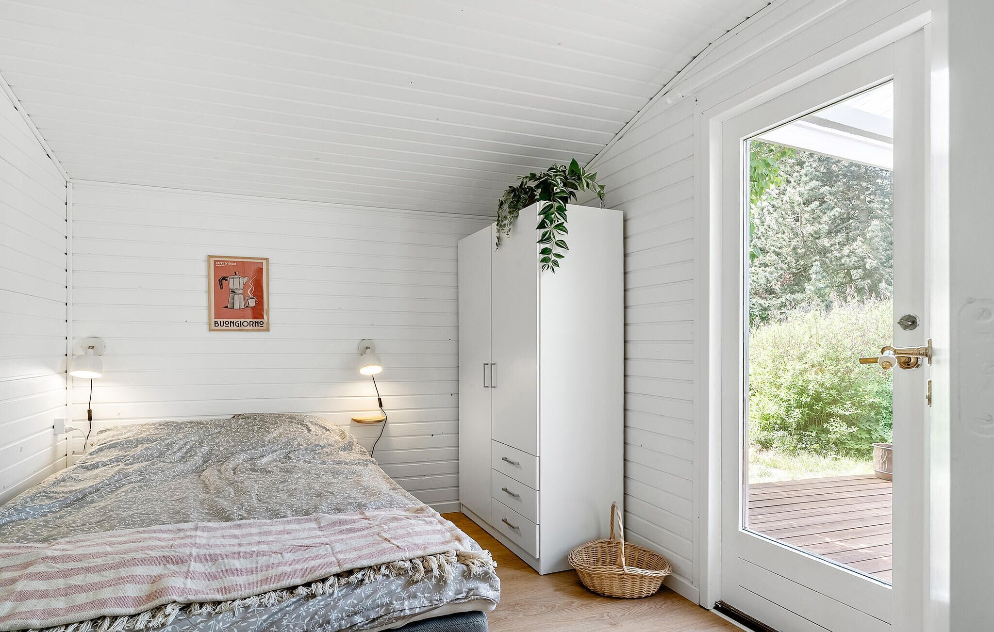 Quarto com cama, luminárias de cabeceira, guarda-roupa e porta que dá para uma área externa.