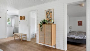 Une pièce avec un plancher en bois, une armoire en rotin, un lit recouvert d’une couverture à motifs et un mur orné d’une affiche représentant un marché aux fruits.