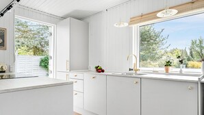 Une cuisine moderne avec des meubles blancs, une grande fenêtre et un évier doté d’un robinet doré.