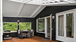 Un patio extérieur abrité, doté d’une terrasse en bois, d’une table avec des chaises et d’un barbecue.